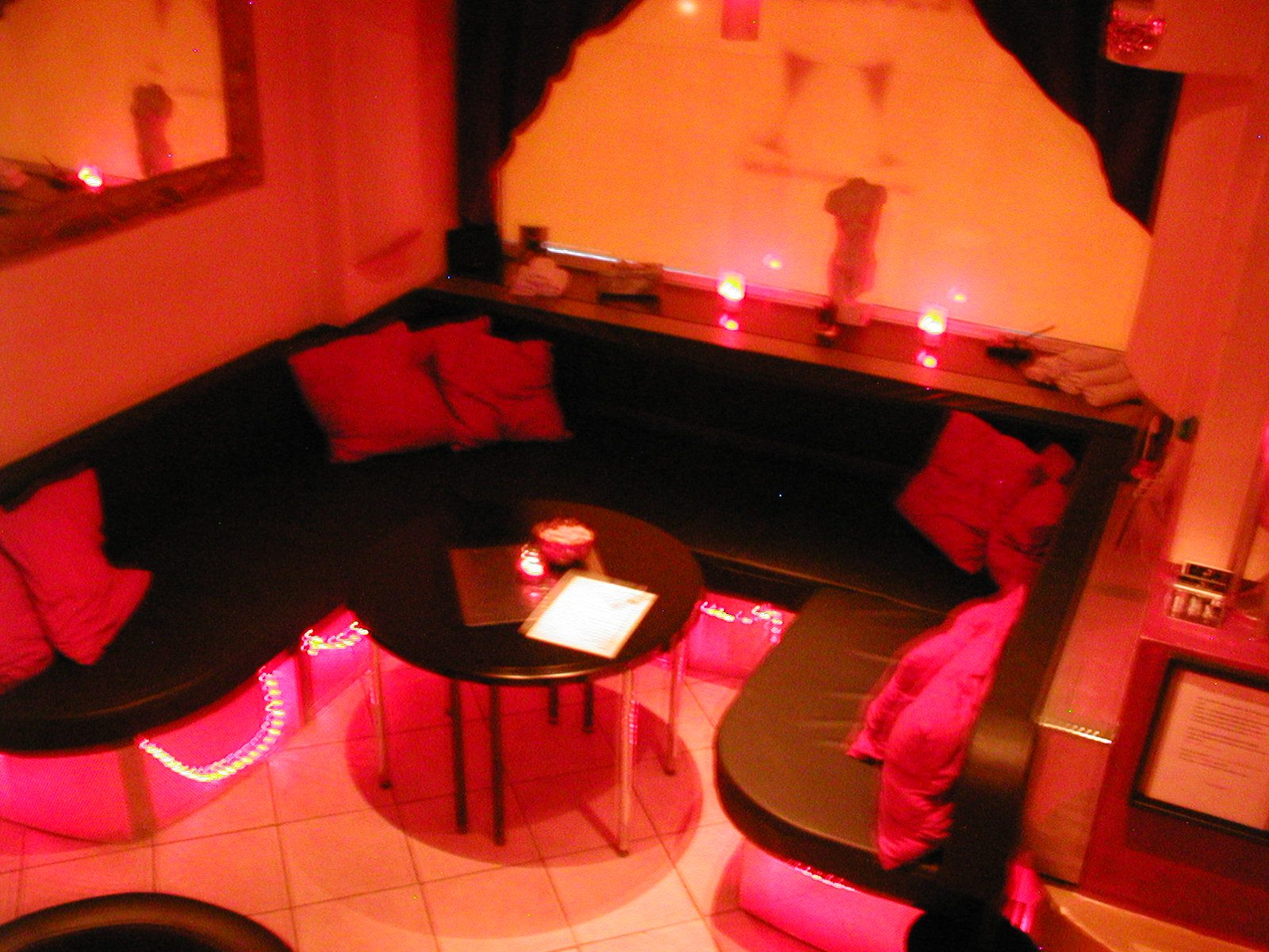 Ecksofa mit roten Kissen und rundem Tisch in rotem Licht.