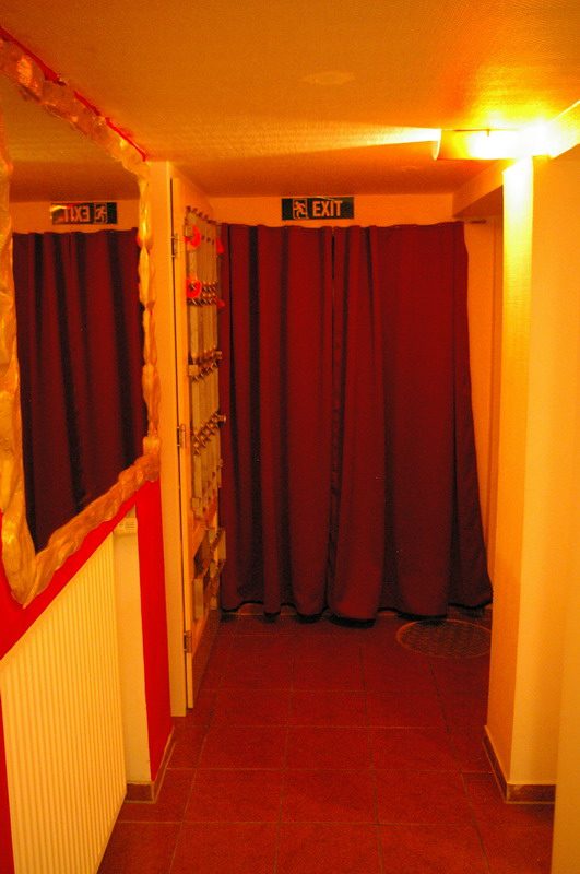 Flur mit rotem Vorhang, Spind und grünem EXIT-Schild.